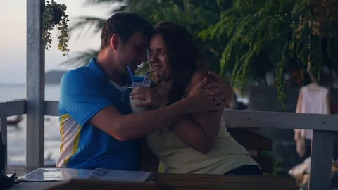 A nice young couple is sitting in a cafe at sunset, the girl is drinking a Stock Footage 88264190