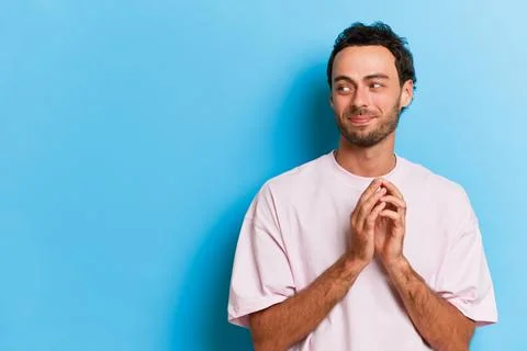 Nice young man with beard standing on blue background in white T-shirt, looking Stock Photos