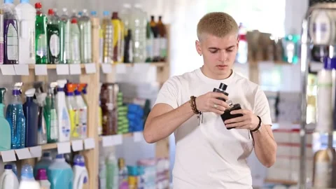 Nice young man customer buying perfume and choosing between two bottle in store Vidéo 332638136