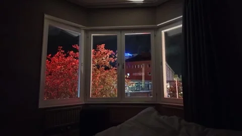 Night Bay Window Scene with Red Trees, Neon Sign, and Bed in Foreground Stock Footage 347682271