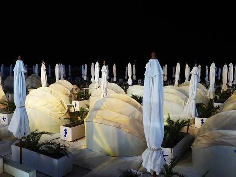 Night beach with many semicircular sofas with awnings and folded umbrellas 스톡 사진