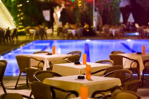 Night cafe, empty tables served for dinner, candles, lights, by the pool in t Stock Photos