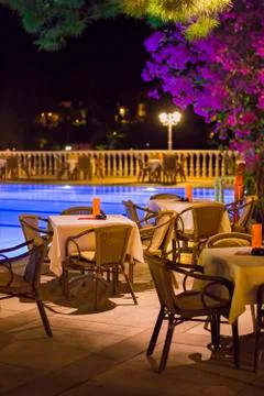 Night cafe, empty tables served for dinner, candles, lights, by the pool in t Stock Photos
