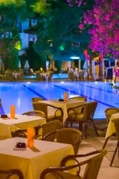 Night cafe, empty tables served for dinner, candles, lights, by the pool in t Stock Photos