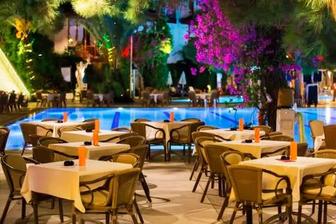 Night cafe, empty tables served for dinner, candles, lights, by the pool in t Stock Photos
