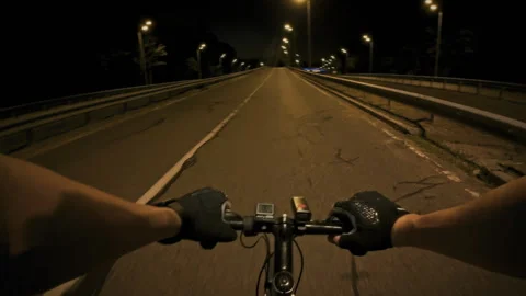 Night cycling on an empty road with city lights illuminating the path ahead Stock Footage 323867523