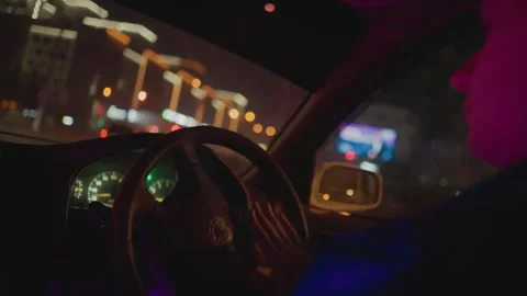 Night driver turning steering wheel under neon city lights reflections on Video stock 329454374