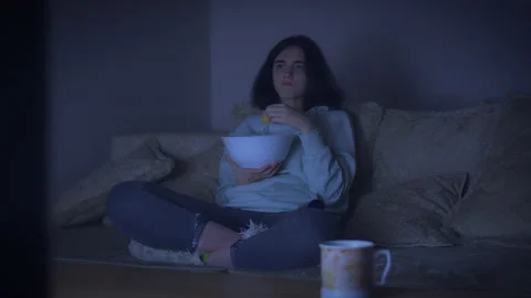 At night, a girl eats potato chips from a large bowl, watches TV, switching Stock Footage 164332242