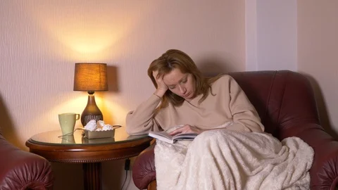 At night the girl reads the book under a blanket on a chair. she falls asleep Видео 88339853