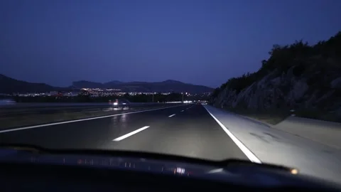 Night highway driving toward distant city lights through mountain landscape Stockbeeldmateriaal 341622926