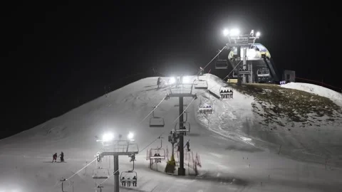 A night-lit ski slope with a functioning chairlift, skiers preparing at the top. Video stock 297707448