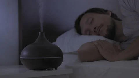 At night man slips in bed with an aromatherapy diffuser working on a nightstand Video stock 149251021
