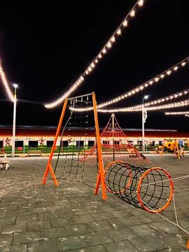 Night at the outdoor playground with glowing string lights, orange climbing.. Stock Photos