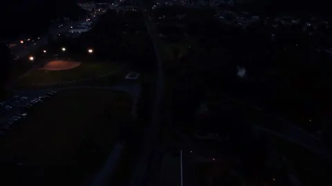 Night overhead forward shot of a park, baseball field, and surrounding town Stock Footage 247428178