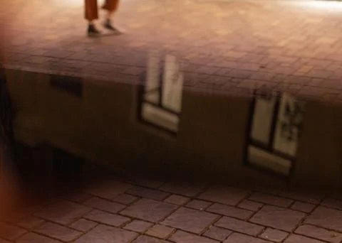 Night puddle reflection on cobblestone street with walking feet Stock Photos