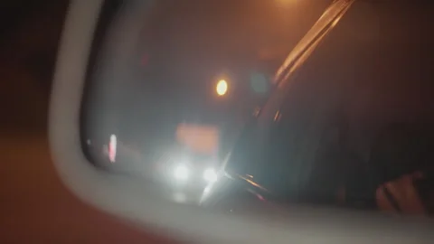 Night rearview mirror shows soft beams and city bokeh, lone passenger watches Stock Footage 324957841