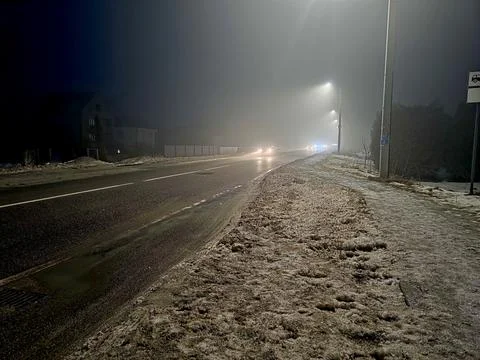 Night Road Covered in Snow With Distant Lights Shining Through Fog and Mist Stock Photos
