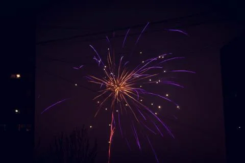 Night salute. Explosion lines of different colors. Outbreaks between houses. Stock Photos