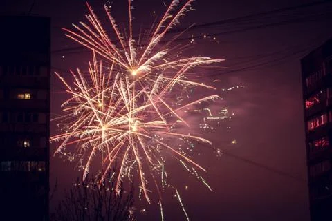 Night salute. Explosion lines of different colors. Outbreaks between houses. Stockfoto's
