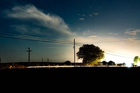 Night scene with clouds, power lines, and distant lights in a rural area ne.. Stock Photos