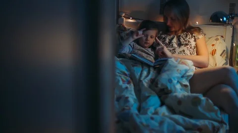 Night scene Overall plan. Mom reads her little daughter a fairy tale before bedt Stock Footage 98858801
