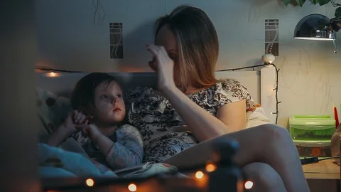 Night scene Overall plan. Mom reads her little daughter a fairy tale before bedt Stock-Footage 98858844