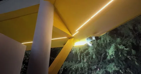 Night shot of yellow LED structure with pine trees and security cameras Stock Footage 340550860