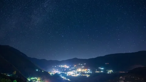 Night sky time lapse with a town in the middle of mountains in the foreground. Stock-Footage 264151709