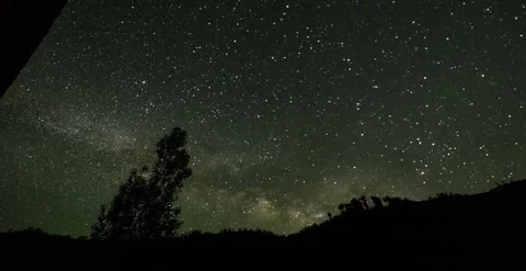 Night sky with tree in forground, mountains, stars timelapse Видео 247134137