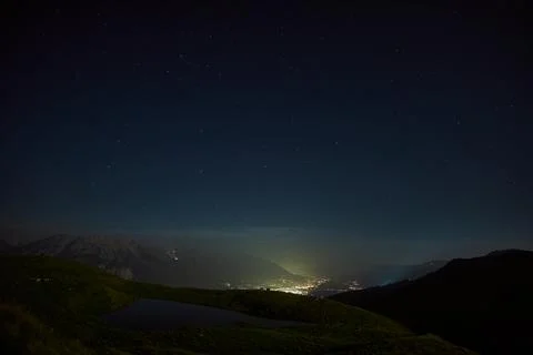 Night sky view over a tranquil valley lit by distant lights from a small town Stock Photos