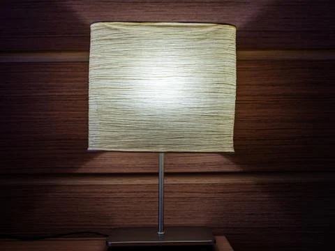 Night table lamp glows on a background of a brown wooden wall Stock Photos