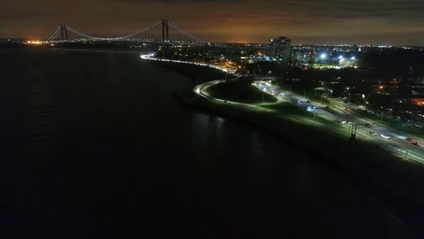 Night traffic streams along the shore below the Verrazzano-Narrows Bridge Stock Footage 76909035