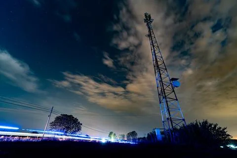 Night view of a cell tower with cloud patterns and a vehicle passing by und.. Stock Photos