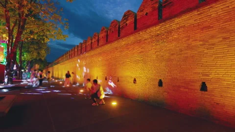 Night view of colorfully lit castle wall in Chiang Mai with people walking Stock Footage 342338989
