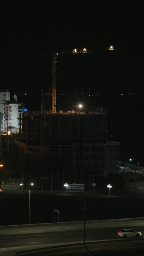 A night view of a high-rise building under construction with a tall tower cra Stock Footage 345019666