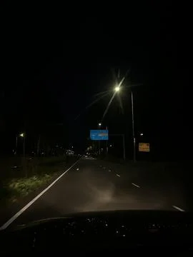 Night view from inside car looking at illuminated Amsterdam direction road sign Stock Photos