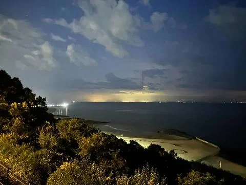 Night view of ocean coast with cloudy sky and distant lightning Stock Photos