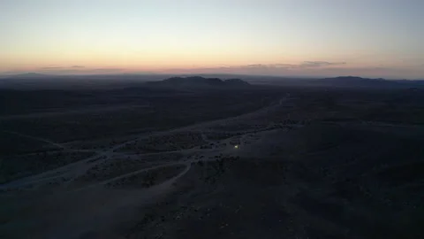 Nighttime aerial of distant car headlights driving through desert on dirt Stock Footage 195200450