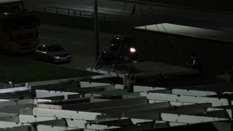 Nighttime construction work with crane lifting large building panel, workers Stock Footage 344864747
