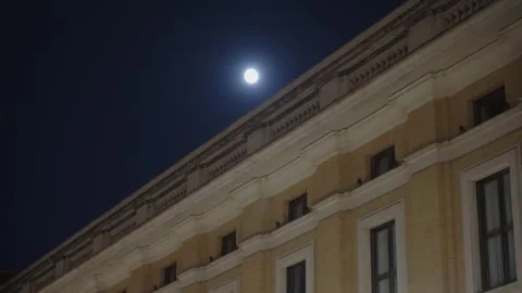 Nighttime full moon glows beside stately brick building, highlighting its Видео 348102422