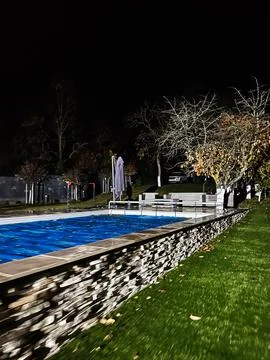Nighttime poolside scene with stone wall edging and benches by the water in.. Stock Photos