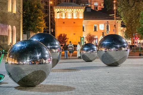 Nighttime scene in a public square or park, with evenly spaced metallic spher Stock Photos