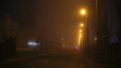 Nighttime shot featuring a lone car driving through a dense fog-filled Stock Footage 324704400