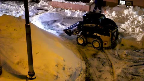 Nighttime snow removal operation with compact loader and street lighting Stock Footage 331506144