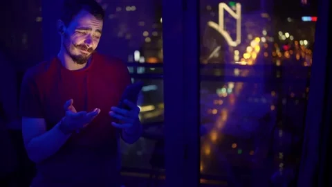 Nighttime tech reflection, Focused individual uses smartphone near window amid Stock Footage 325614264