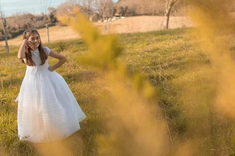 Niña pequeña con vestido blanco de primera comunión sonriendo en un parque Stock Photos