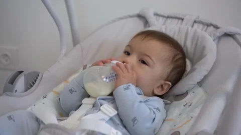 A nine-month-old boy eats milk from a bottle while lying in a cradle swing. The Stock Footage 220904665