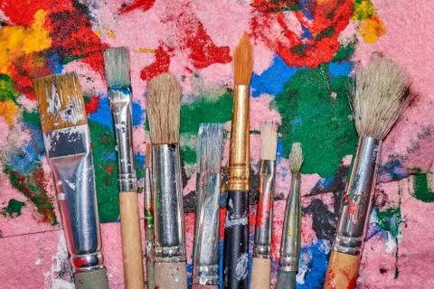 Nine worn out brushes of different sizes on the colorful pink palette Foto stock