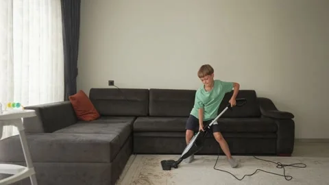 Nine year boy having fun while cleaning. A boy holds a vacuum cleaner like a Stock Footage 194988468