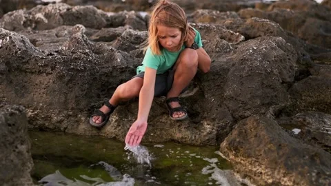 A nine-year-old boy with long, light hair agilely leaps along the rocky seaside Video stock 250826780
